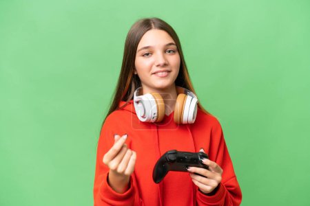 Teenager caucasian girl playing with a video game controller over isolated background making money gesture