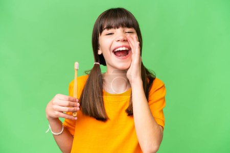 Little caucasian girl brushing teeth over isolated background shouting with mouth wide open