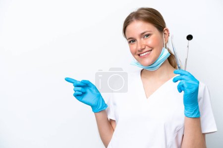 Photo for Dentist caucasian woman holding tools isolated on white background pointing finger to the side - Royalty Free Image
