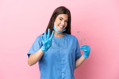 Téléchargez les photos : Dentiste femme tenant des outils isolés sur fond rose heureux et comptant quatre avec les doigts - en image libre de droit