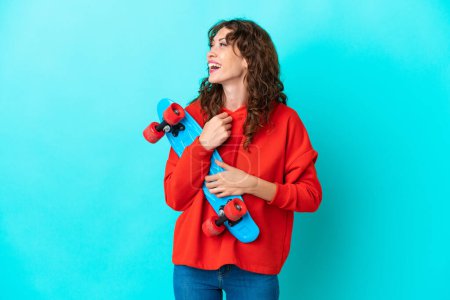 Photo for Young woman with curly hair isolated on blue background with a skate with happy expression - Royalty Free Image