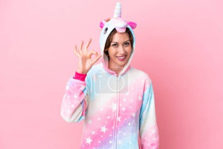Téléchargez les photos : Jeune femme caucasienne avec pyjama licorne isolé sur fond rose montrant ok signe avec les doigts - en image libre de droit