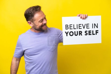 Photo for Middle age caucasian man isolated on yellow background holding a placard with text Believe In Your Self - Royalty Free Image