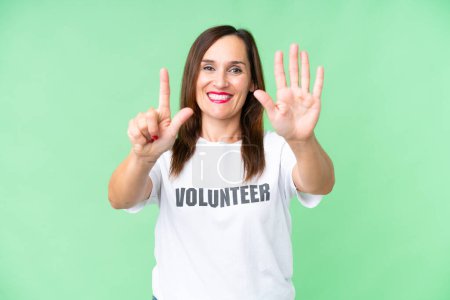 Freiwillige Frau mittleren Alters über isolierten Chroma-Schlüssel-Hintergrund, der sieben mit den Fingern zählt