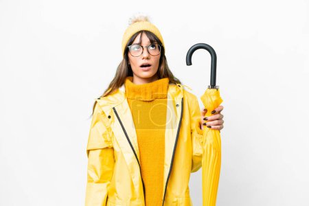 Téléchargez les photos : Young caucasian woman with rainproof coat and umbrella over isolated white background looking up and with surprised expression - en image libre de droit