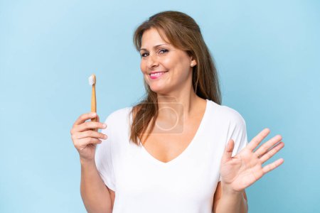 Foto de Middle-aged caucasian woman brushing teeth isolated on blue background saluting with hand with happy expression - Imagen libre de derechos