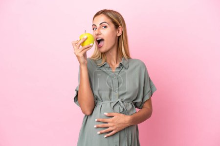 Photo for Young Uruguayan woman isolated on blue background pregnant and holding an apple - Royalty Free Image