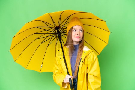 Téléchargez les photos : Jeune jolie femme avec manteau imperméable et parapluie sur fond isolé chroma clé et la recherche vers le haut - en image libre de droit