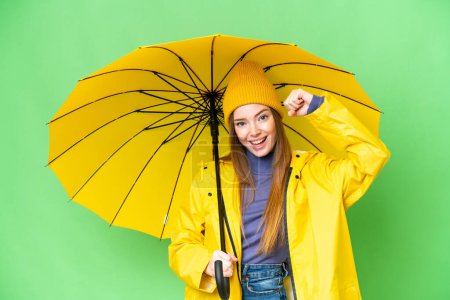 Téléchargez les photos : Jeune jolie femme avec manteau imperméable et parapluie sur fond de chroma isolé célébrant une victoire - en image libre de droit
