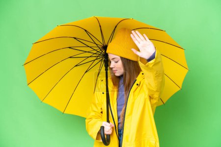 Téléchargez les photos : Jeune jolie femme avec manteau imperméable et parapluie sur fond isolé chroma clé faisant geste d'arrêt et déçu - en image libre de droit