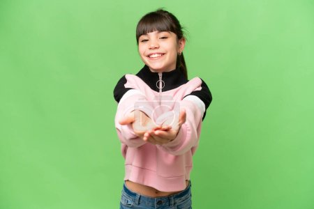 Photo for Little girl over isolated green chroma key background holding copyspace imaginary on the palm to insert an ad - Royalty Free Image