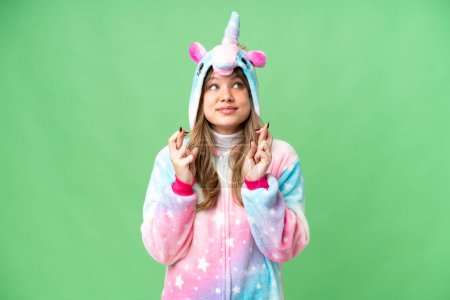 Foto de Chica joven con pijama de unicornio sobre fondo de croma clave aislado con los dedos cruzando - Imagen libre de derechos