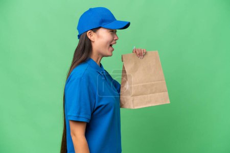 Foto de Young Asian woman taking a bag of takeaway food over isolated background laughing in lateral position - Imagen libre de derechos