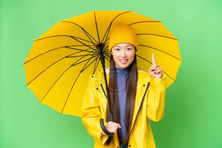 Téléchargez les photos : Young Asian woman with rainproof coat and umbrella over isolated chroma key background pointing up a great idea - en image libre de droit