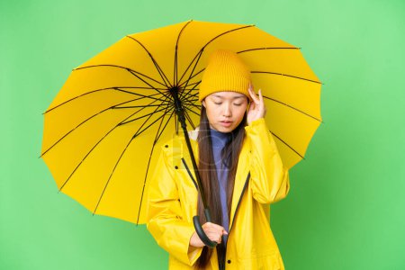 Téléchargez les photos : Young Asian woman with rainproof coat and umbrella over isolated chroma key background with headache - en image libre de droit