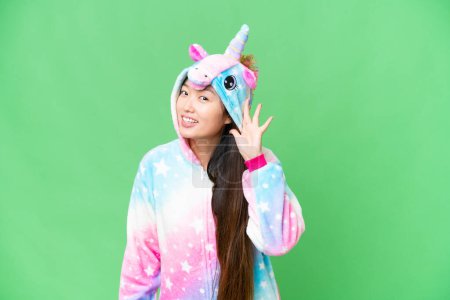 Foto de Young Asian woman with unicorn pajamas over isolated chroma key background listening to something by putting hand on the ear - Imagen libre de derechos