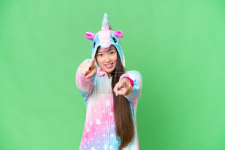 Foto de Young Asian woman with unicorn pajamas over isolated chroma key background points finger at you while smiling - Imagen libre de derechos