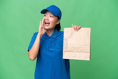 Foto de Young Asian woman taking a bag of takeaway food over isolated background shouting with mouth wide open to the side - Imagen libre de derechos