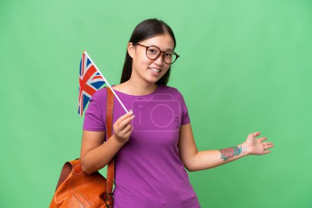 Téléchargez les photos : Young Asian woman holding an United Kingdom flag over isolated background extending hands to the side for inviting to come - en image libre de droit
