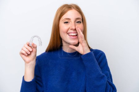 Young redhead woman holding invisible braces isolated on white background shouting with mouth wide open