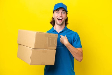 Delivery handsome man isolated on yellow background with surprise facial expression