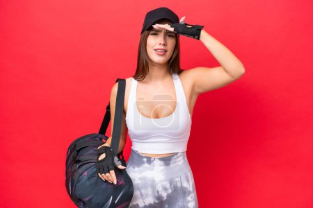 Photo for Young beautiful sport woman with sport bag isolated on red background looking far away with hand to look something - Royalty Free Image