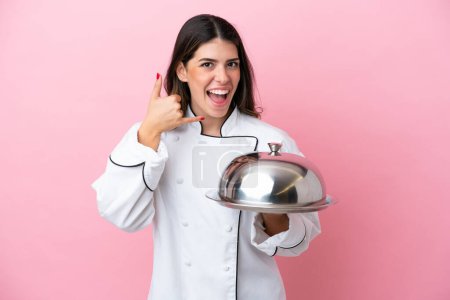 Foto de Young Italian chef woman holding tray with lid isolated on pink background making phone gesture. Call me back sign - Imagen libre de derechos