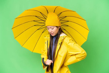 Téléchargez les photos : Young Asian woman with rainproof coat and umbrella over isolated chroma key background suffering from backache for having made an effort - en image libre de droit