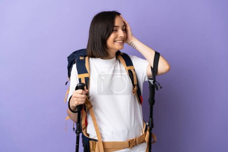Junge kaukasische Frau mit Rucksack und Trekkingstöcken auf blauem Hintergrund, die viel lächelt