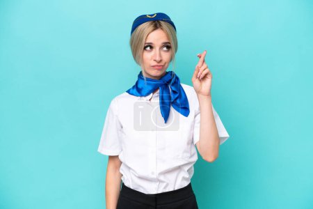 Photo for Airplane blonde stewardess woman isolated on blue background with fingers crossing and wishing the best - Royalty Free Image