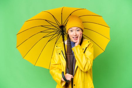 Téléchargez les photos : Young Asian woman with rainproof coat and umbrella over isolated chroma key background with surprise and shocked facial expression - en image libre de droit