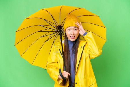 Téléchargez les photos : Young Asian woman with rainproof coat and umbrella over isolated chroma key background with surprise expression - en image libre de droit