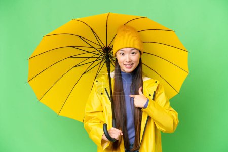 Téléchargez les photos : Young Asian woman with rainproof coat and umbrella over isolated chroma key background with surprise facial expression - en image libre de droit