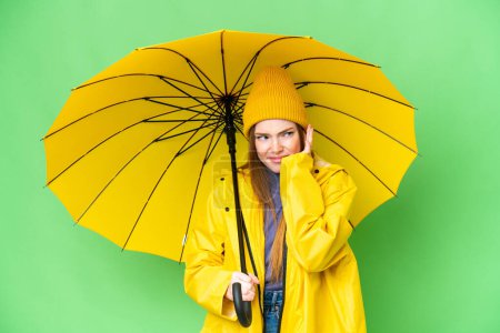 Téléchargez les photos : Young pretty woman with rainproof coat and umbrella over isolated chroma key background frustrated and covering ears - en image libre de droit