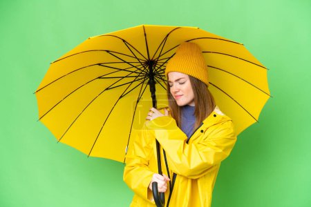 Téléchargez les photos : Young pretty woman with rainproof coat and umbrella over isolated chroma key background suffering from pain in shoulder for having made an effort - en image libre de droit