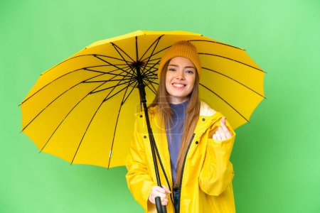 Téléchargez les photos : Young pretty woman with rainproof coat and umbrella over isolated chroma key background making money gesture - en image libre de droit
