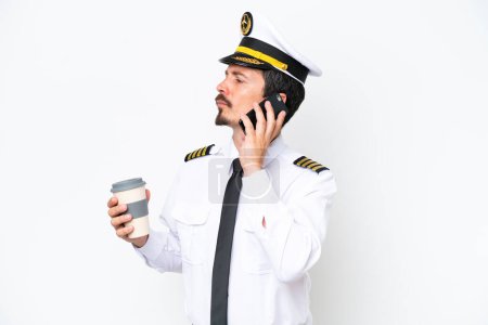 Photo for Airplane caucasian pilot isolated on white background holding coffee to take away and a mobile - Royalty Free Image