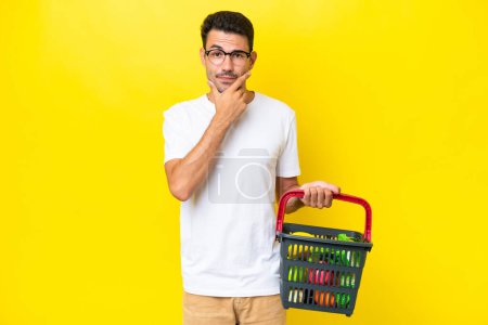 Photo for Young handsome man holding a shopping basket full of food over isolated yellow background thinking - Royalty Free Image