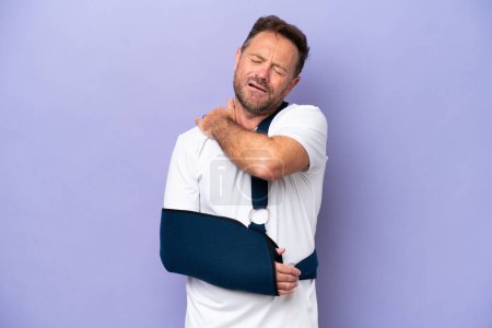 Téléchargez les photos : Middle age caucasian man with broken arm and wearing a sling isolated on purple background suffering from pain in shoulder for having made an effort - en image libre de droit