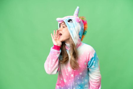 Foto de Chica joven con pijama de unicornio sobre fondo de croma clave aislado gritando con la boca abierta hacia el lateral - Imagen libre de derechos