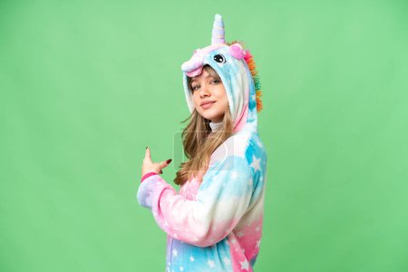 Foto de Chica joven con pijama de unicornio sobre fondo de croma clave aislado apuntando hacia atrás - Imagen libre de derechos