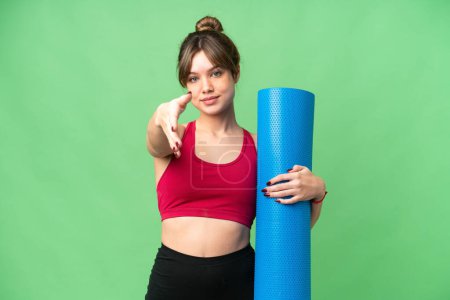 Foto de Joven chica deportiva que va a clases de yoga mientras sostiene una estera sobre un fondo de croma clave aislado estrechando las manos para cerrar una buena oferta - Imagen libre de derechos