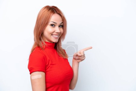 Foto de Joven chica rusa con curitas aisladas sobre fondo rosa sorprendida y señalando con el dedo hacia un lado - Imagen libre de derechos