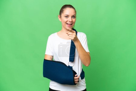 Photo for Young blonde woman with broken arm and wearing a sling over isolated chroma key background surprised and pointing front - Royalty Free Image