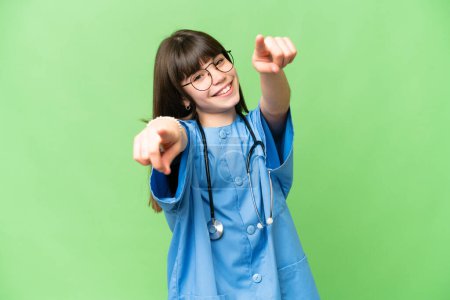 Little girl as a surgeon doctor over isolated chroma key background points finger at you while smiling