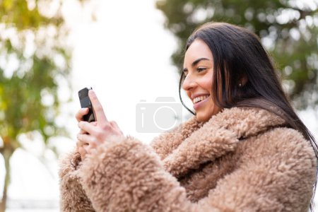 Junge Frau benutzt Handy im Freien mit glücklichem Gesichtsausdruck