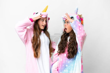 Foto de Amigos chicas con pijama de unicornio sobre fondo blanco aislado con sorpresa y expresión facial impactada - Imagen libre de derechos