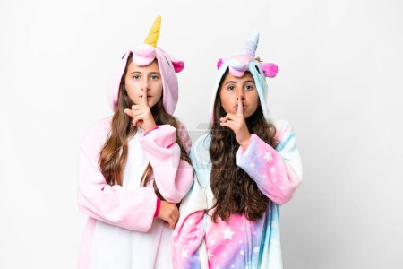 Foto de Amigos chicas con pijama de unicornio sobre fondo blanco aislado mostrando un gesto de silencio poniendo el dedo en la boca - Imagen libre de derechos