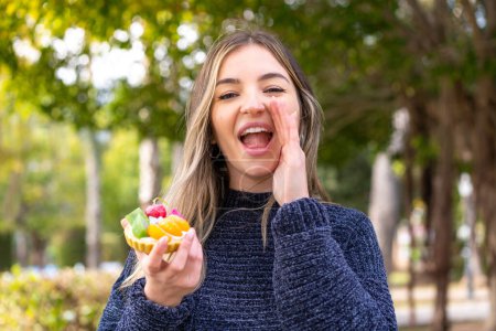 Young pretty Romanian woman holding a tartlet at outdoors shouting with mouth wide open
