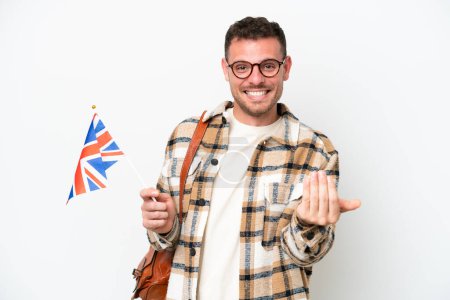 Téléchargez les photos : Jeune hispanique tenant un drapeau du Royaume-Uni isolé sur fond blanc invitant à venir avec la main. Heureux que tu sois venu - en image libre de droit